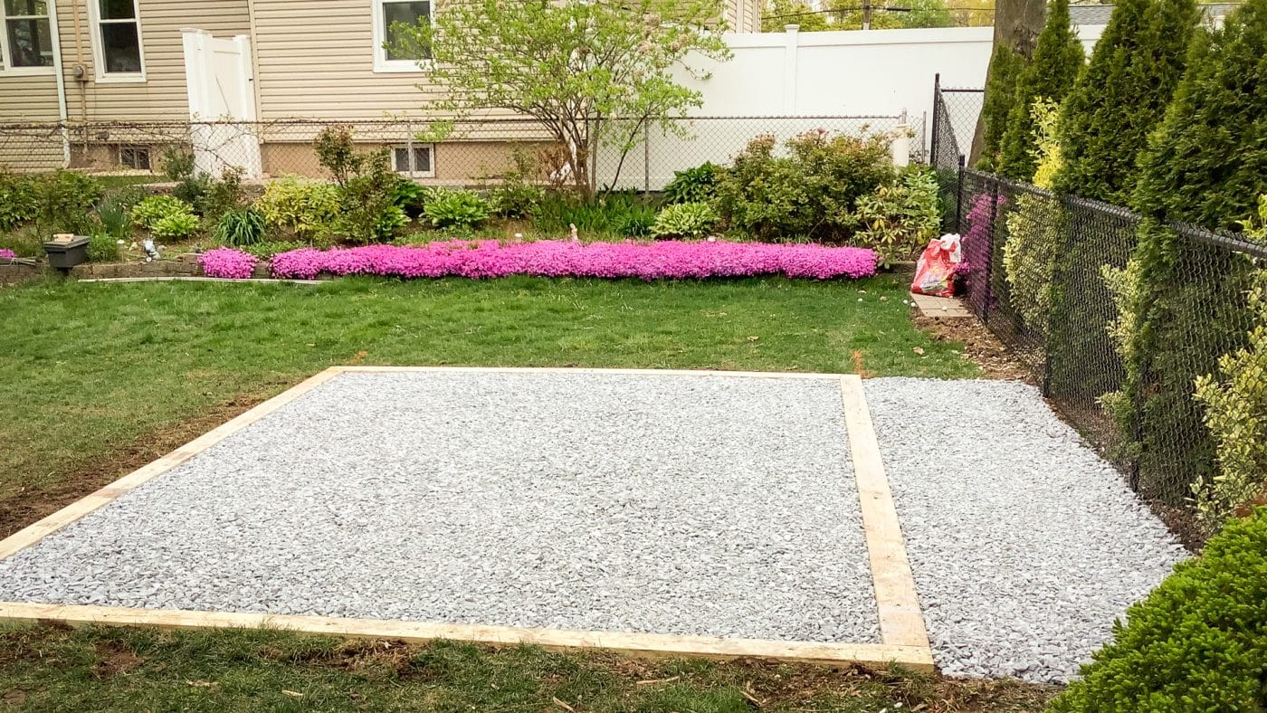 A fire pit gravel patio area in a backyard beside flower beds