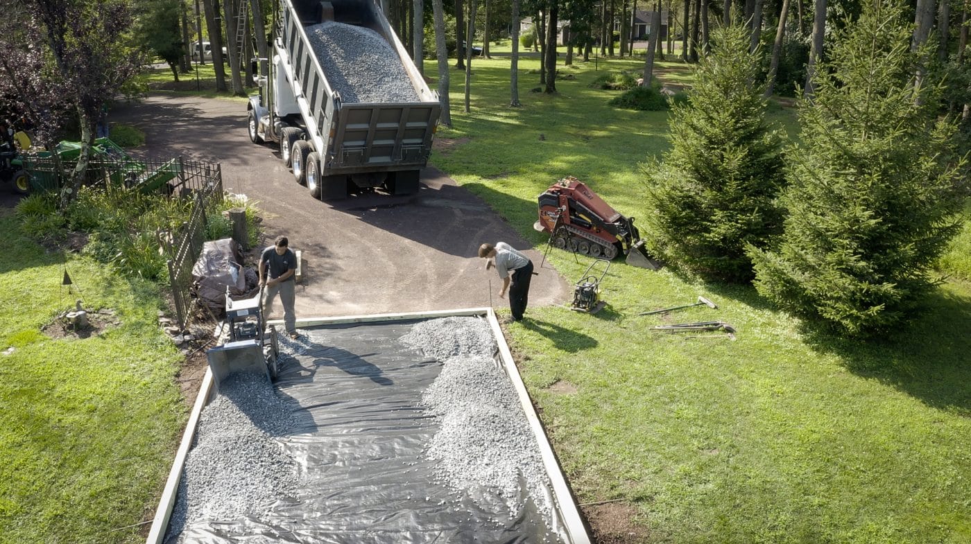 aerial view of men pouring gravel on foundation for a step in the how to build a shed base on uneven ground process