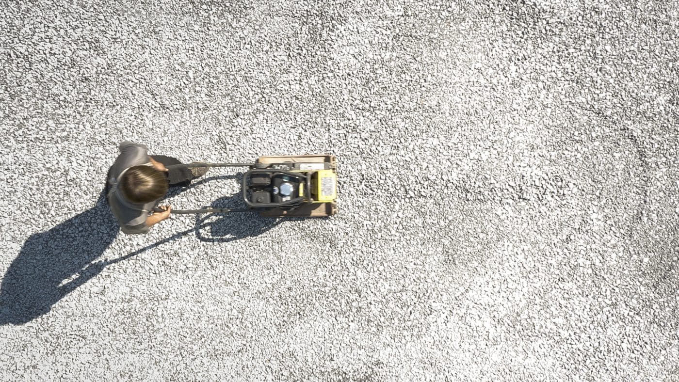 aerial view of man tamping gravel as a step on how to build a shed base on uneven ground