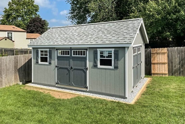 A grey shed anchored into gravel.