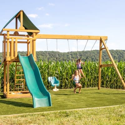 children swinging on swings on turf swingset base foundation